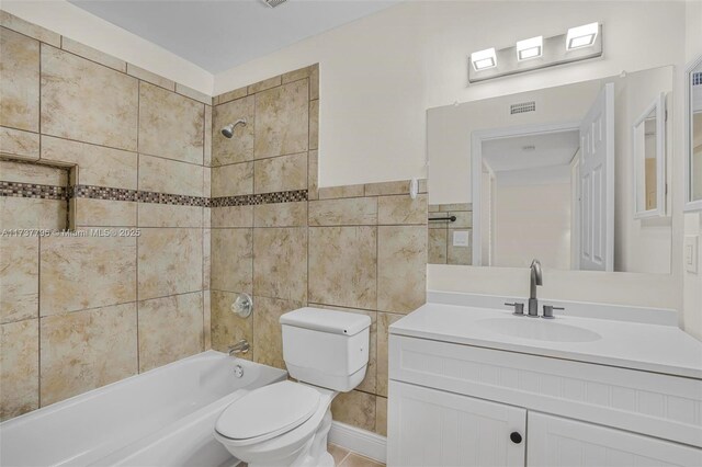 full bathroom featuring tiled shower / bath combo, vanity, tile walls, and toilet