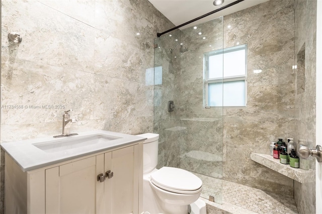 full bath with a tile shower, tile walls, toilet, and vanity