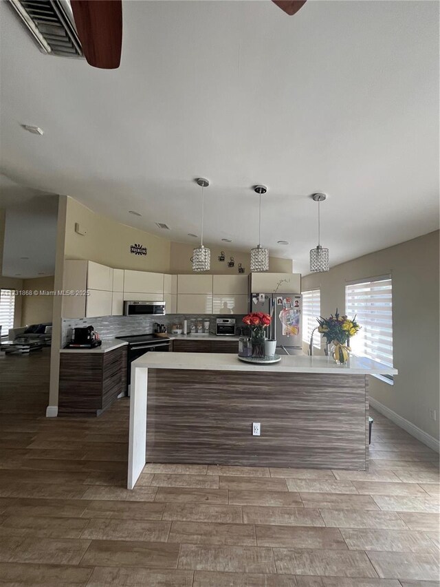 kitchen with appliances with stainless steel finishes, light hardwood / wood-style flooring, white cabinetry, hanging light fixtures, and decorative backsplash