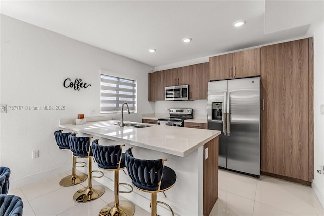 kitchen featuring sink, appliances with stainless steel finishes, light stone counters, a kitchen bar, and light tile patterned flooring