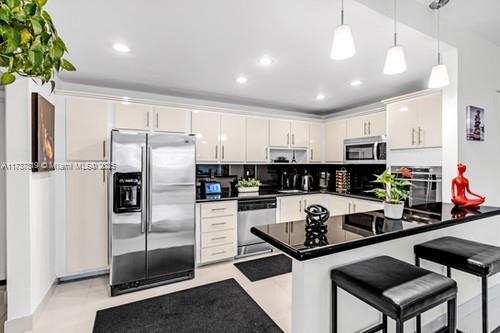 kitchen featuring appliances with stainless steel finishes, a breakfast bar area, decorative backsplash, hanging light fixtures, and kitchen peninsula