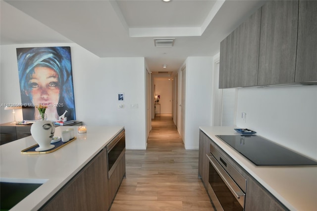 kitchen with stainless steel appliances, a raised ceiling, and light wood-type flooring