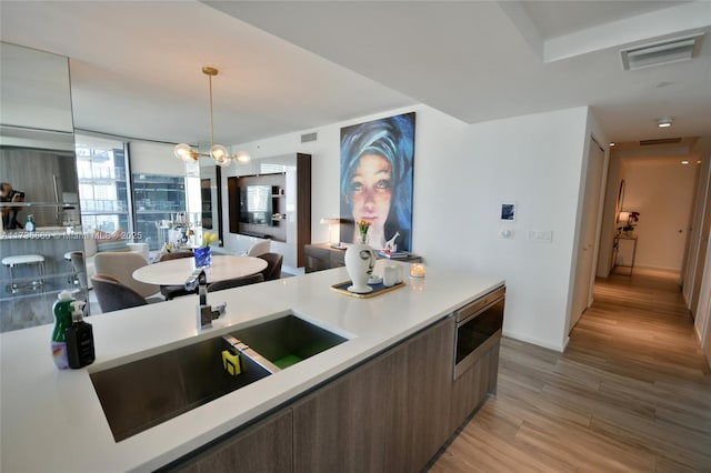 kitchen with sink, an inviting chandelier, light wood-type flooring, stainless steel microwave, and pendant lighting