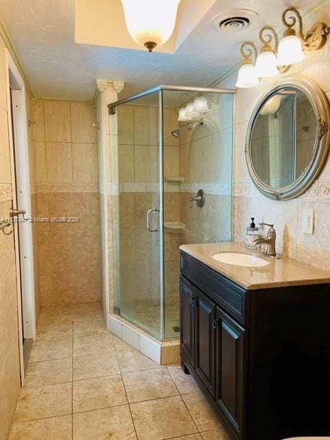 bathroom featuring tile patterned flooring, vanity, tile walls, and a shower with shower door