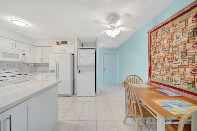 kitchen featuring stacked washer / dryer, a textured ceiling, white cabinets, and white appliances