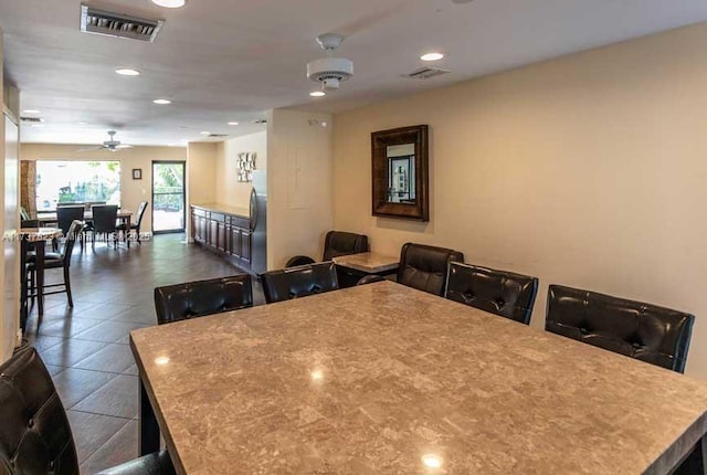 kitchen with a breakfast bar area, stainless steel fridge, a kitchen island, dark tile patterned floors, and ceiling fan