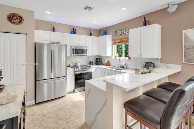 kitchen with appliances with stainless steel finishes, sink, white cabinets, a kitchen breakfast bar, and kitchen peninsula