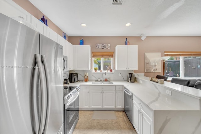 kitchen with appliances with stainless steel finishes, white cabinetry, sink, light tile patterned floors, and kitchen peninsula