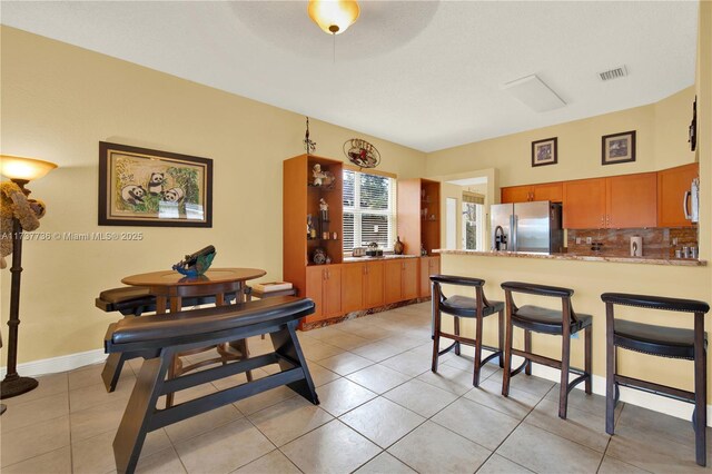 kitchen featuring light tile patterned floors, a breakfast bar, appliances with stainless steel finishes, backsplash, and kitchen peninsula