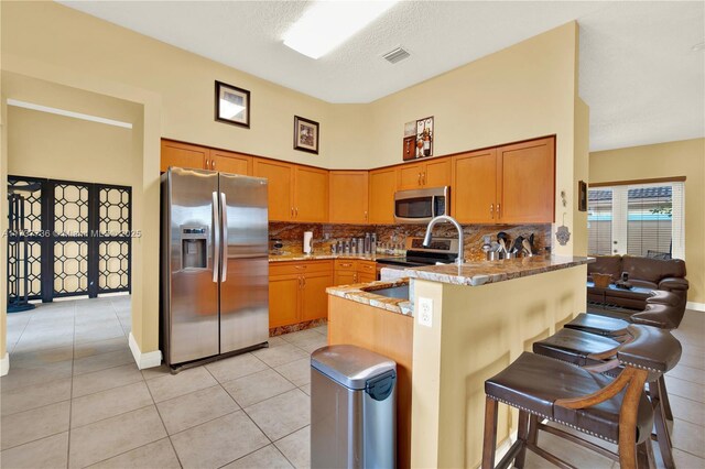 kitchen featuring light tile patterned floors, appliances with stainless steel finishes, tasteful backsplash, a kitchen bar, and kitchen peninsula