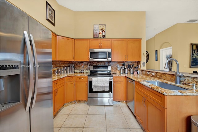 kitchen featuring decorative backsplash, appliances with stainless steel finishes, light stone counters, a peninsula, and a sink