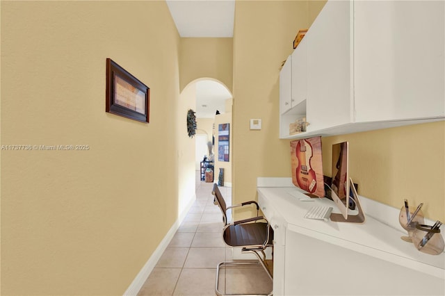 corridor featuring light tile patterned floors, baseboards, and arched walkways