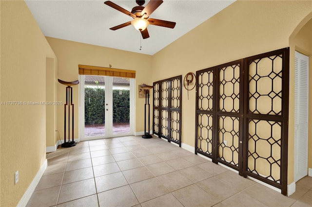 empty room with light tile patterned floors, arched walkways, a ceiling fan, and baseboards