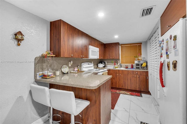 kitchen featuring sink, a breakfast bar area, kitchen peninsula, white appliances, and backsplash