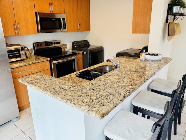 kitchen with appliances with stainless steel finishes, a breakfast bar, washer / dryer, kitchen peninsula, and light stone countertops