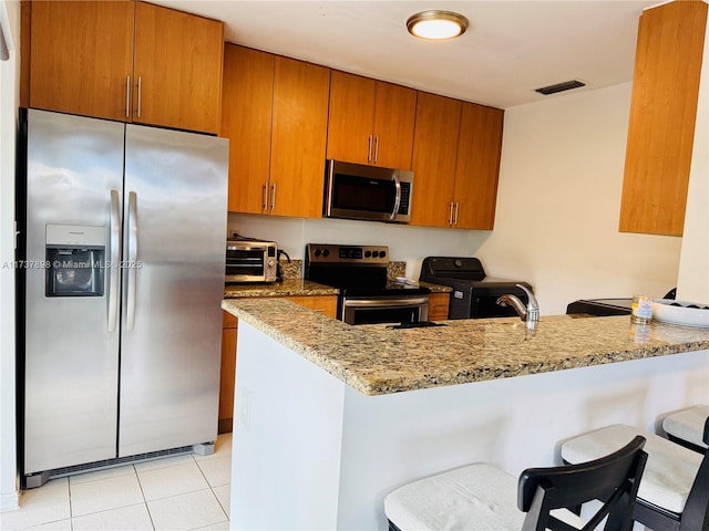 kitchen featuring light stone countertops, a kitchen breakfast bar, stainless steel appliances, and kitchen peninsula