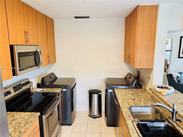 kitchen featuring light stone counters, washing machine and clothes dryer, stainless steel appliances, and sink