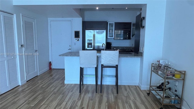 kitchen featuring dark wood-type flooring, a breakfast bar area, light stone countertops, and appliances with stainless steel finishes