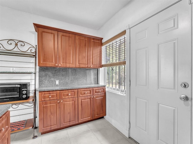 kitchen featuring backsplash, light tile patterned floors, and light stone countertops