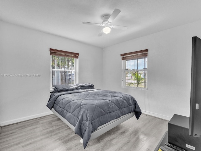 bedroom with ceiling fan, light hardwood / wood-style floors, and multiple windows