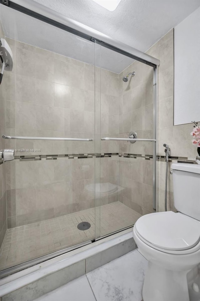 bathroom featuring a textured ceiling, a shower with door, and toilet