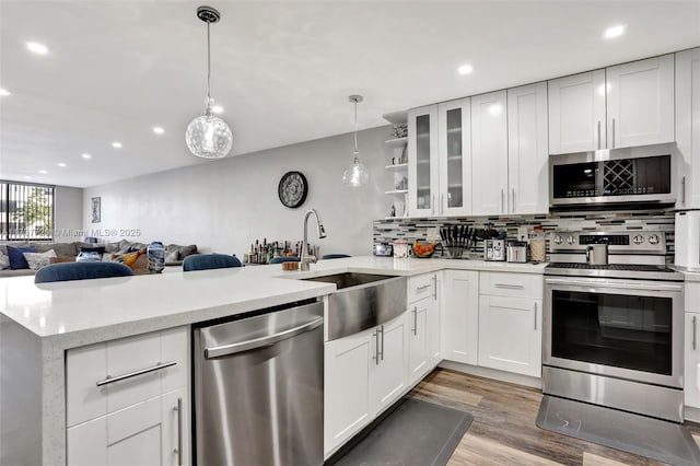 kitchen with decorative light fixtures, sink, white cabinets, kitchen peninsula, and stainless steel appliances