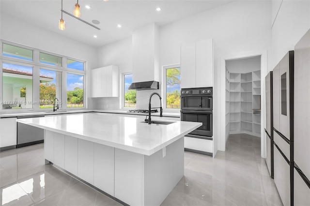 kitchen with pendant lighting, appliances with stainless steel finishes, an island with sink, white cabinets, and wall chimney exhaust hood