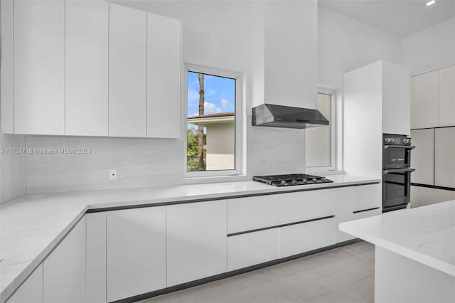 kitchen with double oven, light stone countertops, stainless steel gas cooktop, white cabinets, and decorative backsplash