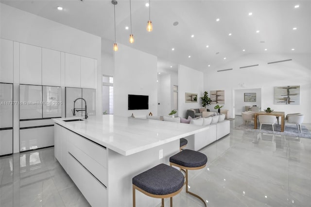 kitchen with sink, a high ceiling, white cabinets, decorative light fixtures, and a large island with sink