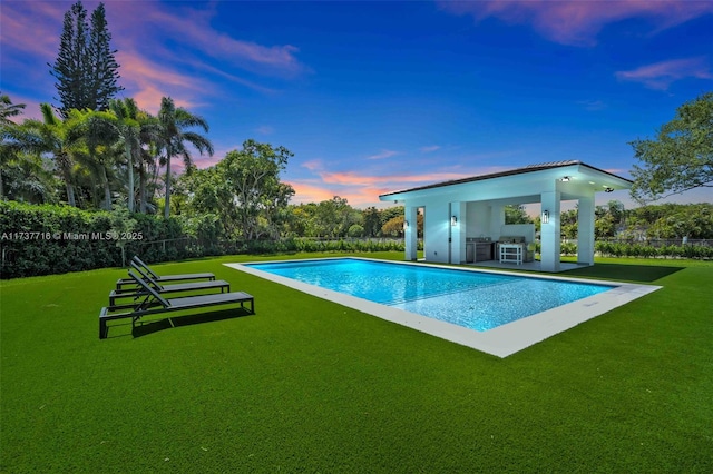 pool at dusk with exterior kitchen and a lawn