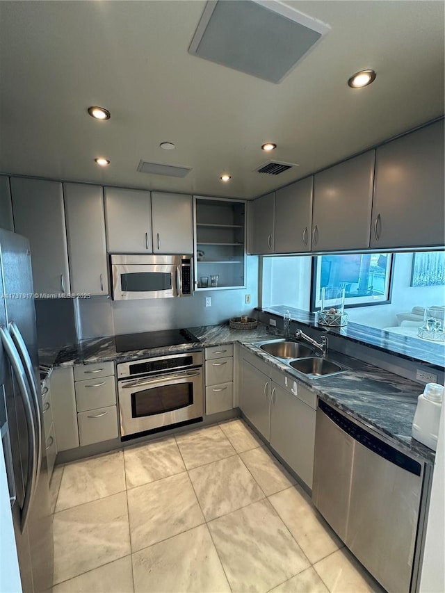 kitchen with stainless steel appliances, sink, dark stone counters, and gray cabinetry