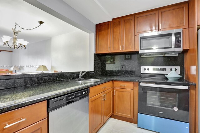 kitchen featuring sink, stainless steel appliances, decorative backsplash, dark stone counters, and a chandelier