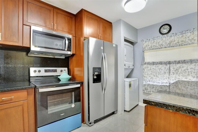 kitchen with stainless steel appliances, stacked washer and dryer, dark stone counters, and decorative backsplash