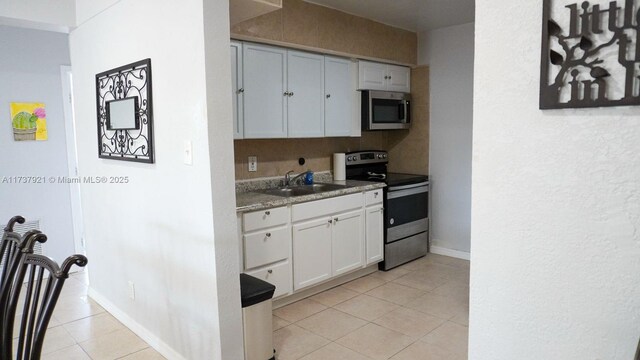 kitchen with light tile patterned flooring, appliances with stainless steel finishes, sink, and white cabinets