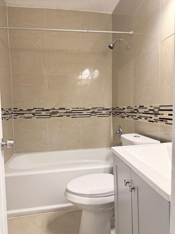 full bathroom with vanity, tiled shower / bath combo, tile walls, and toilet