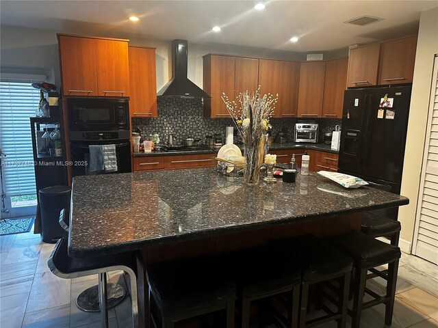 kitchen featuring tasteful backsplash, a breakfast bar area, wall chimney exhaust hood, and black appliances