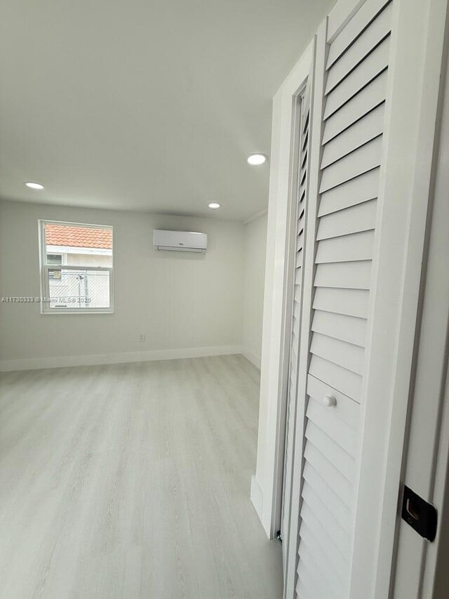 below grade area featuring light wood-type flooring, recessed lighting, a wall unit AC, and baseboards