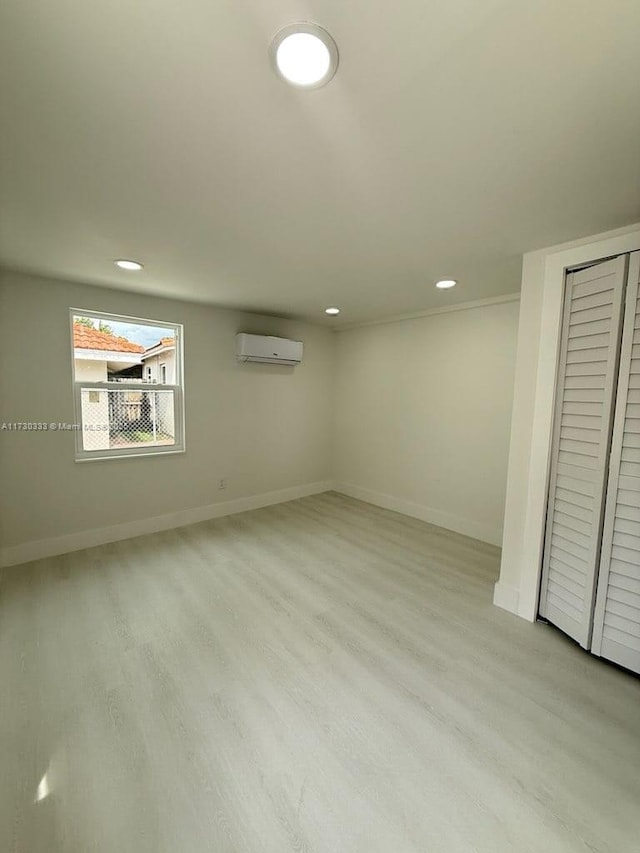 basement with recessed lighting, light wood-style flooring, baseboards, and a wall mounted AC