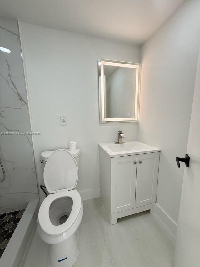 full bathroom featuring toilet, a marble finish shower, baseboards, and vanity