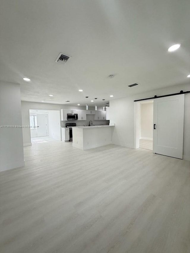 unfurnished living room with light wood-style floors, a barn door, and visible vents