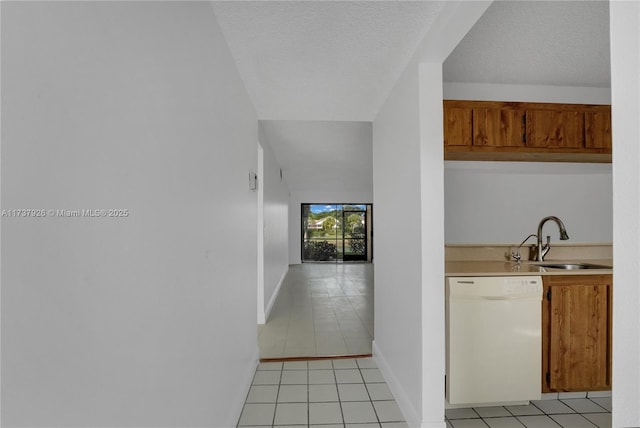 kitchen with dishwasher, sink, light tile patterned flooring, and a textured ceiling