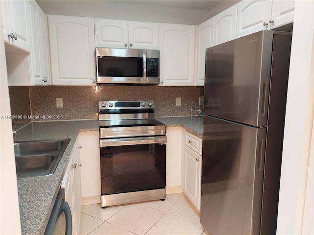 kitchen with appliances with stainless steel finishes, tasteful backsplash, sink, white cabinets, and light tile patterned floors