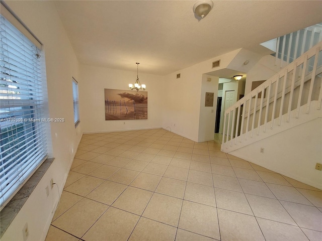 tiled empty room featuring an inviting chandelier