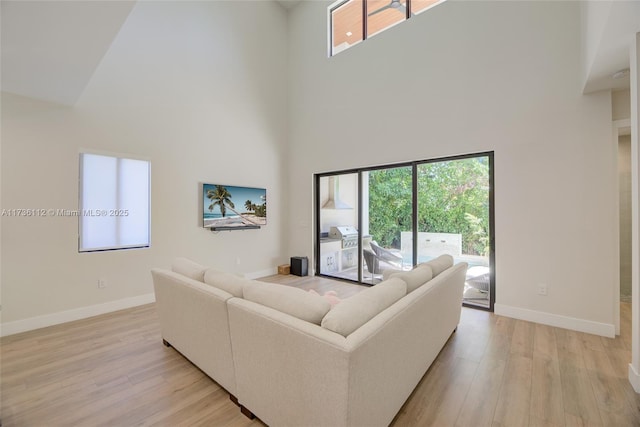 living room featuring a high ceiling, baseboards, and light wood-style floors