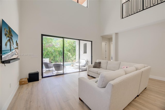 living area featuring light wood finished floors, baseboards, and a towering ceiling