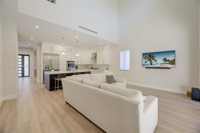 living room featuring a high ceiling, baseboards, light wood finished floors, and recessed lighting