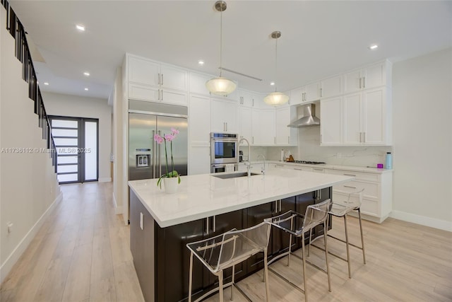kitchen featuring white cabinets, light wood finished floors, stainless steel appliances, tasteful backsplash, and wall chimney range hood