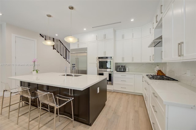 kitchen featuring tasteful backsplash, a breakfast bar area, white cabinets, a kitchen island with sink, and appliances with stainless steel finishes