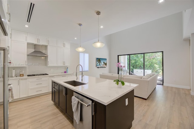 kitchen with sink, stainless steel appliances, an island with sink, decorative light fixtures, and wall chimney exhaust hood