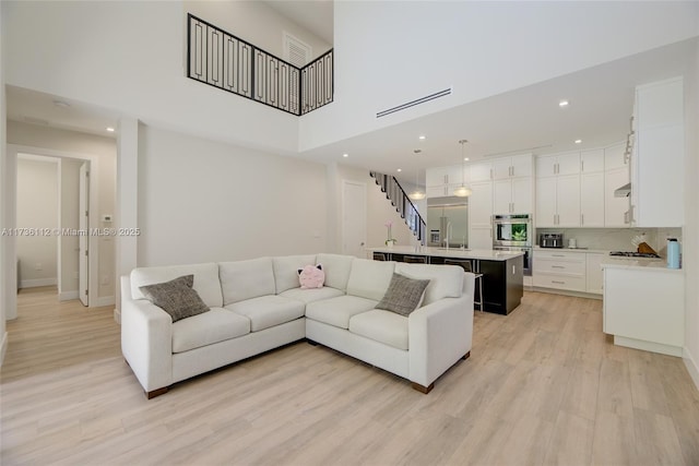 living room featuring a towering ceiling, sink, and light wood-type flooring